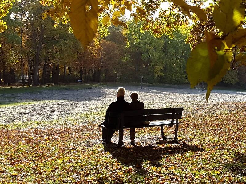 zwei Personen sitzen auf einer Bank in herbstlicher Umgebung