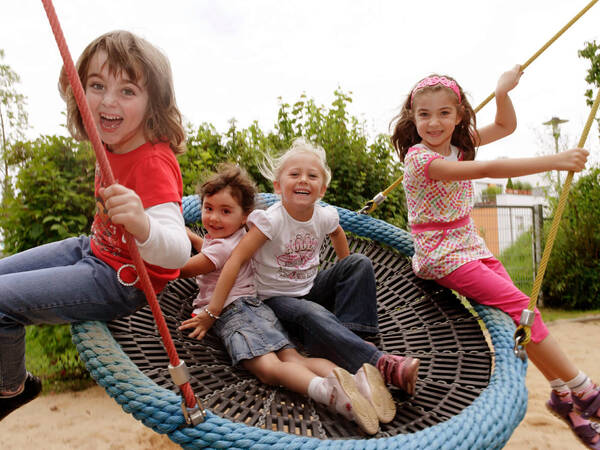 Vier Kinder schaukeln auf einer Nestschaukel.