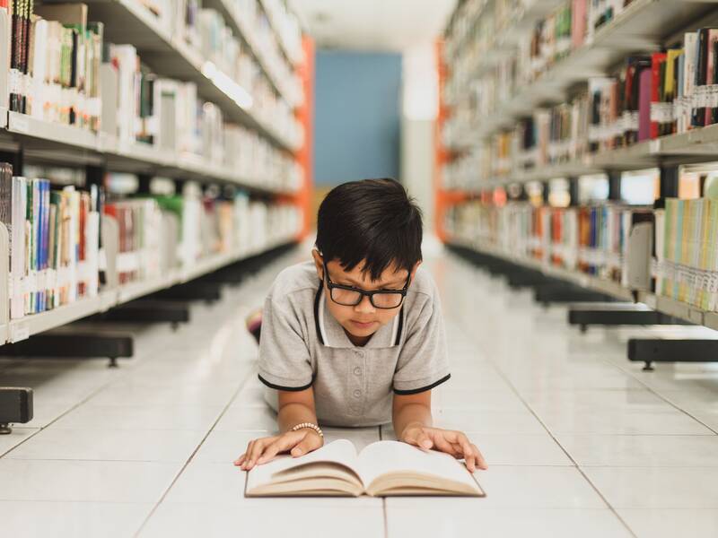 Junge liegt auf dem Boden der Bibliothek und liest ein Buch