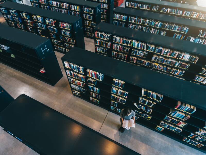 Eine Frau steht in den Gängen einer Bibliothek und wird aus der Vogelperspektive fotografiert.