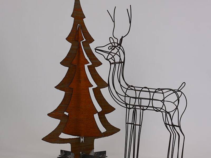 Ein Hirsch aus Draht gemacht steht auf der rechten Seite. Links davon steht ein brauner Tannenbaum aus Rost. 