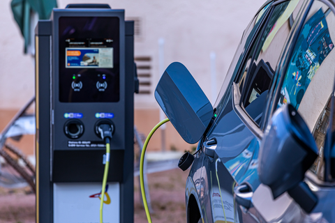 Ladestation für Elektroautos mit einem grün-gelben Kabel. Daneben steht ein Auto welches gerade am Laden ist. 